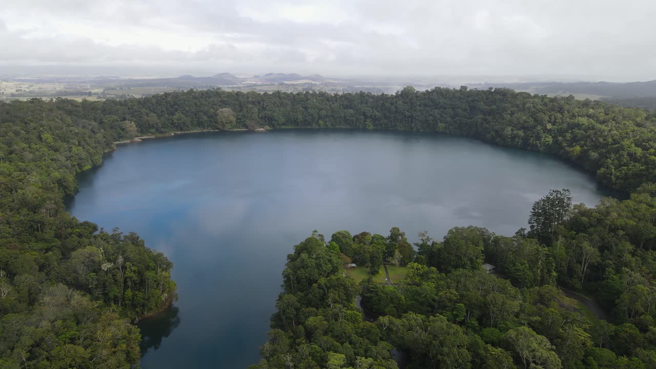 Video drone udara yang menampilkan danau kawah vulkanik besar yang dikelilingi oleh hutan hujan tropis yang rimbun