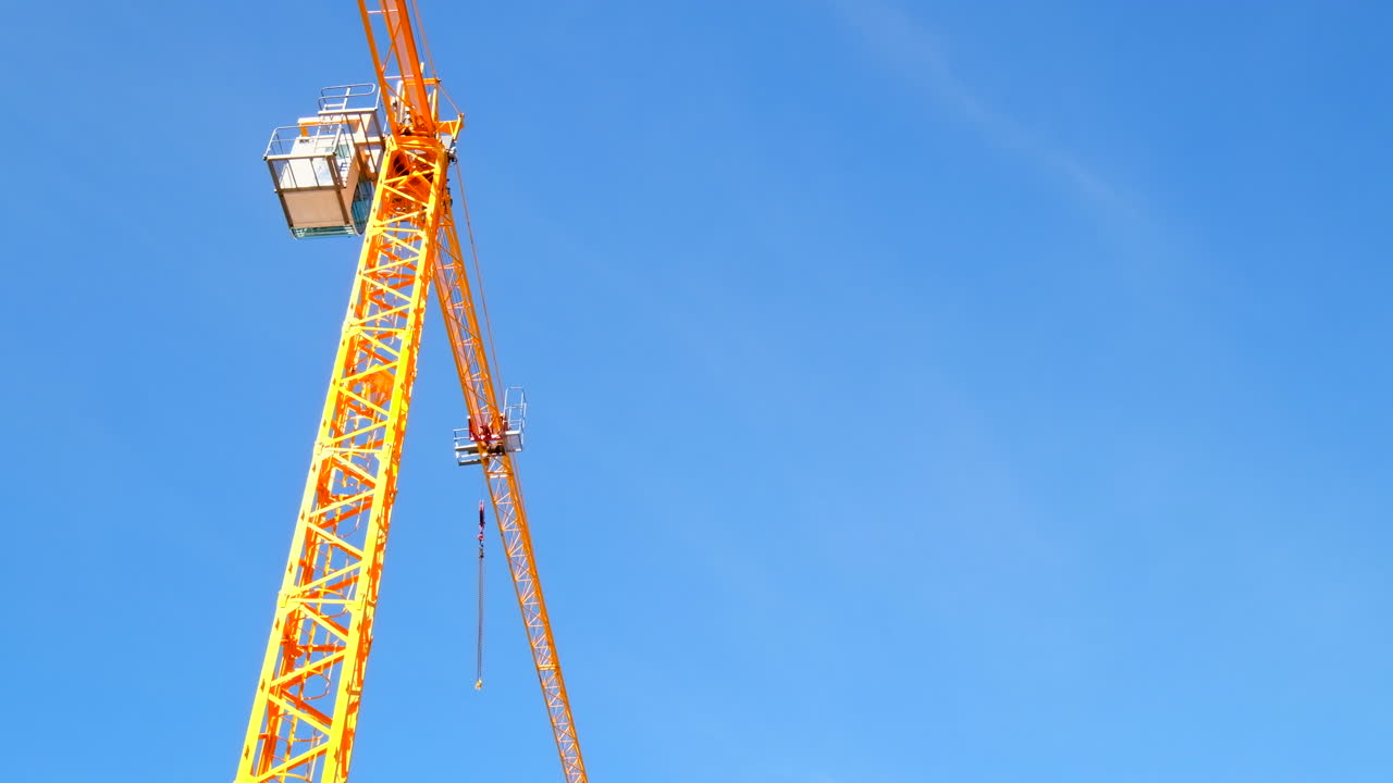 Bright yellow construction crane stands out against blue sky, upward view