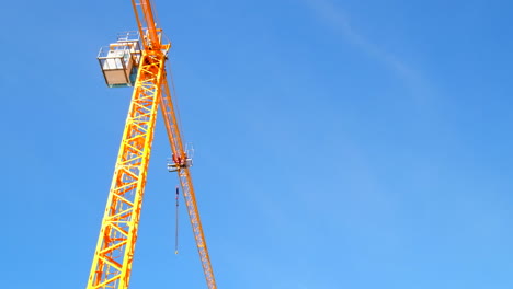 bright yellow construction crane stands out against blue sky, upward view