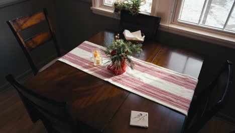 push in shot of a kitchen table with a christmas decoration on top along with a red and white table cloth