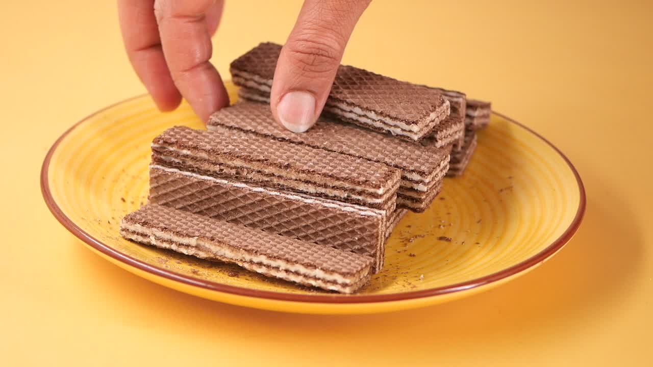 Mano che raccoglie un wafer al cioccolato da un piatto giallo
