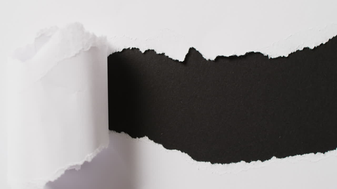 Video of close up of torn piece of white paper on black background
