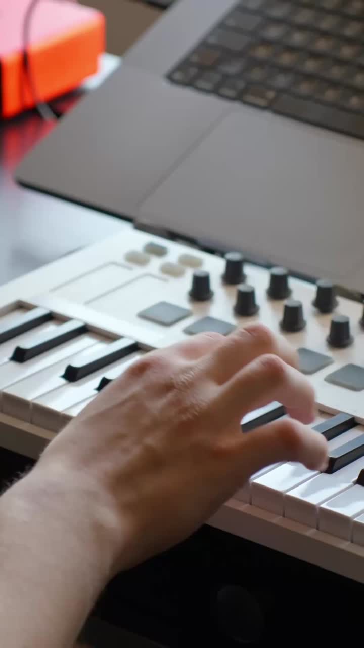 Hand of a music producer performing a melody on a MIDI keyboard controller, creating beats and digital tracks with a laptop for modern electronic music production, vertical static close up