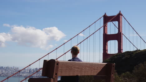 san francisco, california - a young man seated on a bench in close proximity to the golden gate bridge - medium shot