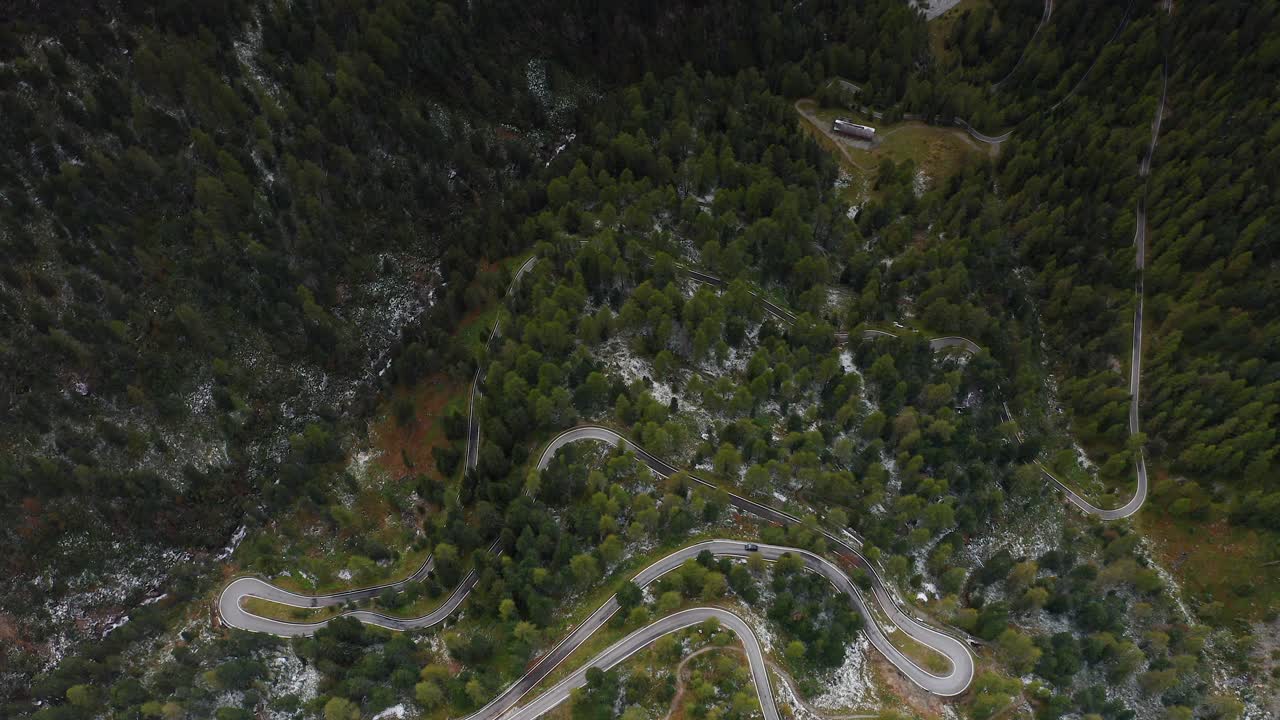 Rising aerial footage above a winding road, a lush green forest, and a crystal clear lake
