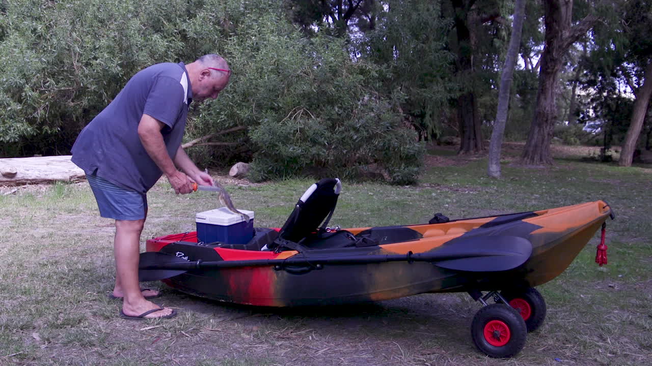 Un pescatore che toglie il suo pescato da una ghiacciaia sul kayak e procede a pulire il pesce.
