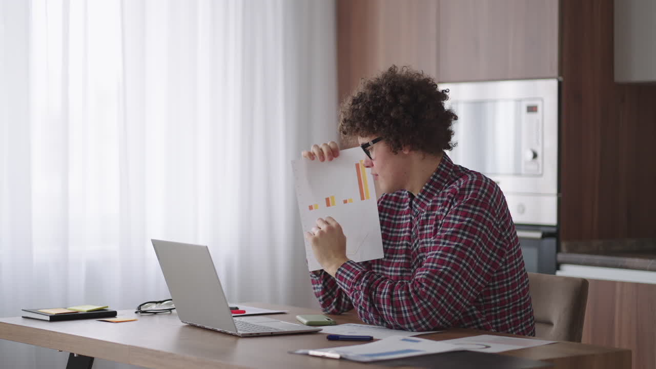 hombre de negocios de cabello rizado con gafas sentado en la oficina desde el escritorio de casa mirando a la cámara y apuntando a una tableta con información financiera mostrada en forma gráfica gráfico de columna