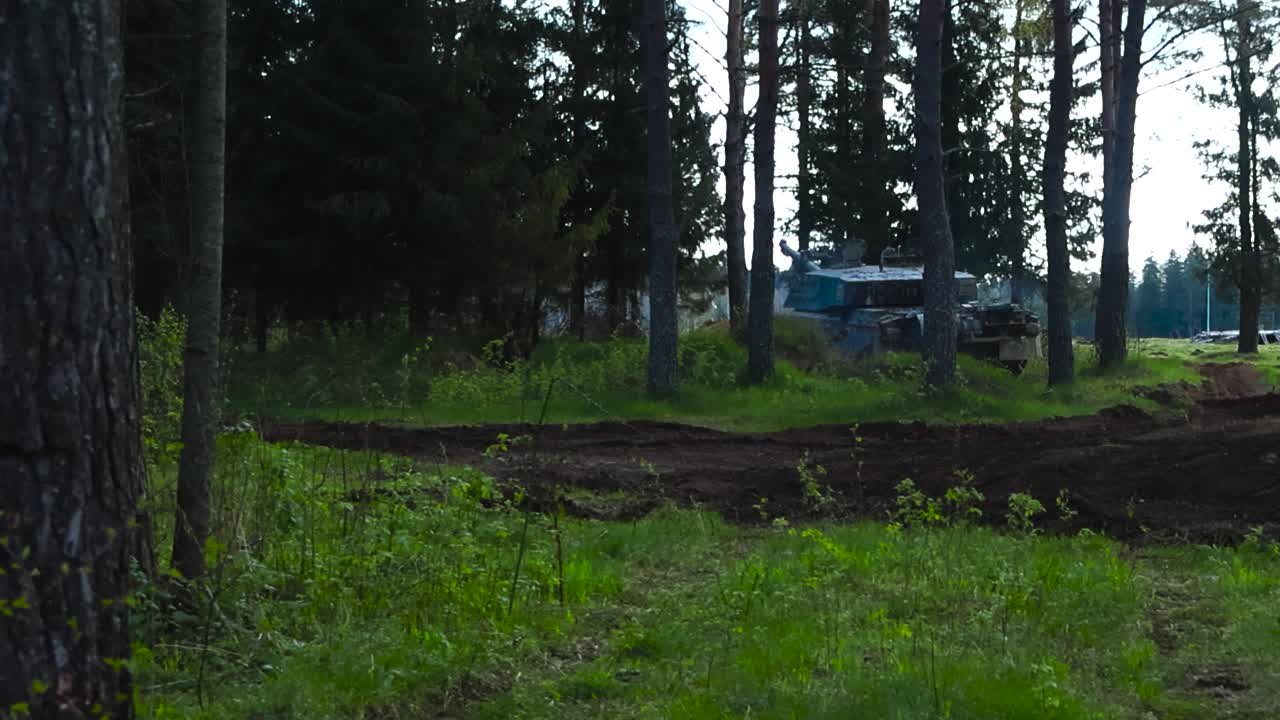 British military Challenger 2 4034 armoured and camouflaged tank hidden and running in a dense and thick vibrant green pine forest during summer cloudy day. Tank is emitting smoke, looks for enemies.