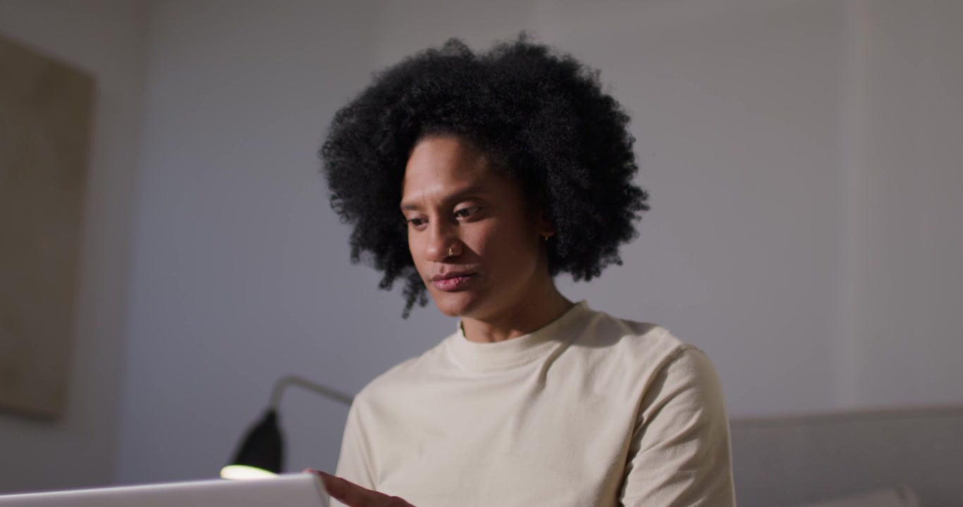 African American adult male placing silver laptop on lap, adjusting screen and working at home
