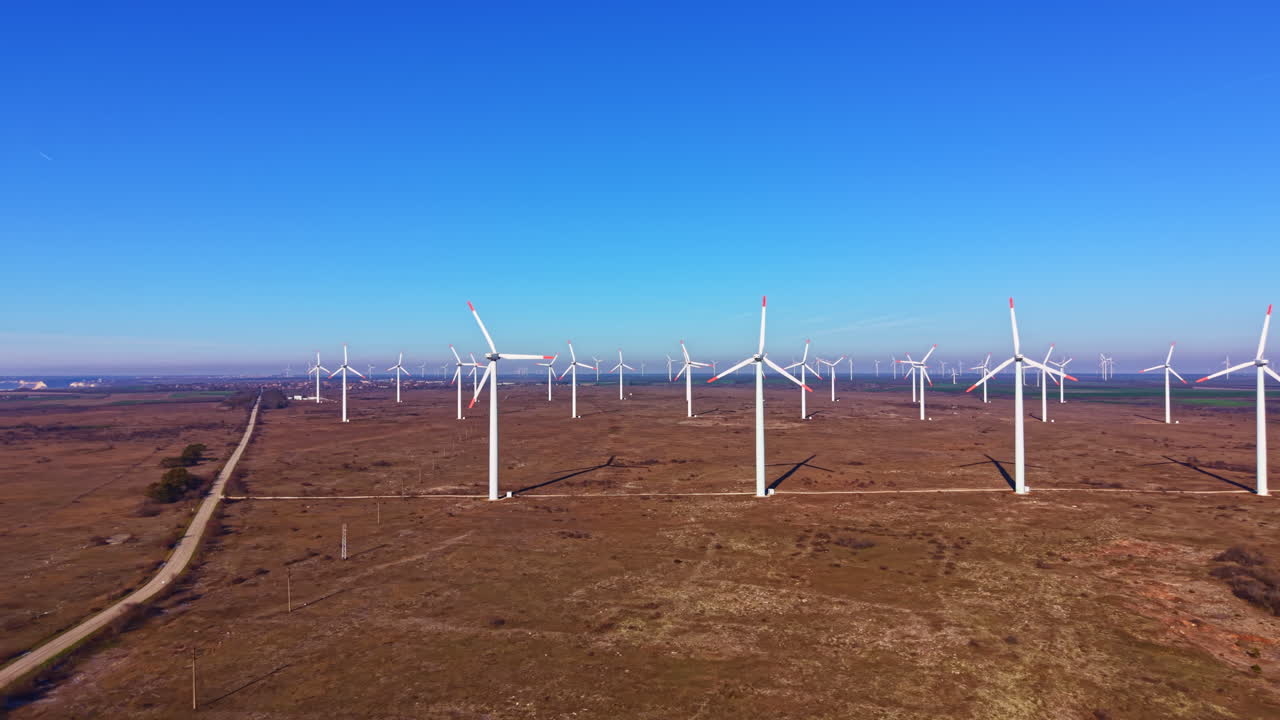 Turbinas eólicas se erguem imponentes em um campo aberto sob um céu azul claro durante o dia, perto de uma área rural.