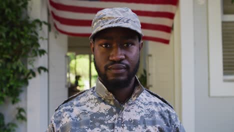 Portrait-of-african-american-male-soldier-standing-in-front-of-house-and-american-flag