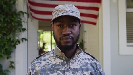 retrato de un soldado afroamericano de pie frente a una casa y una bandera estadounidense