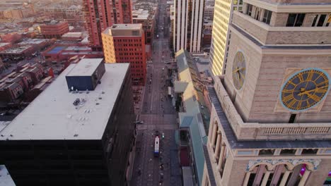 Vista-Aérea-De-Drones-Volando-Por-La-Torre-Del-Reloj-De-Lannies-Panoramización-Hacia-El-Tráfico-De-La-Calle-Arapahoe-En-El-Centro-De-Denver-Colorado-Durante-La-Puesta-De-Sol