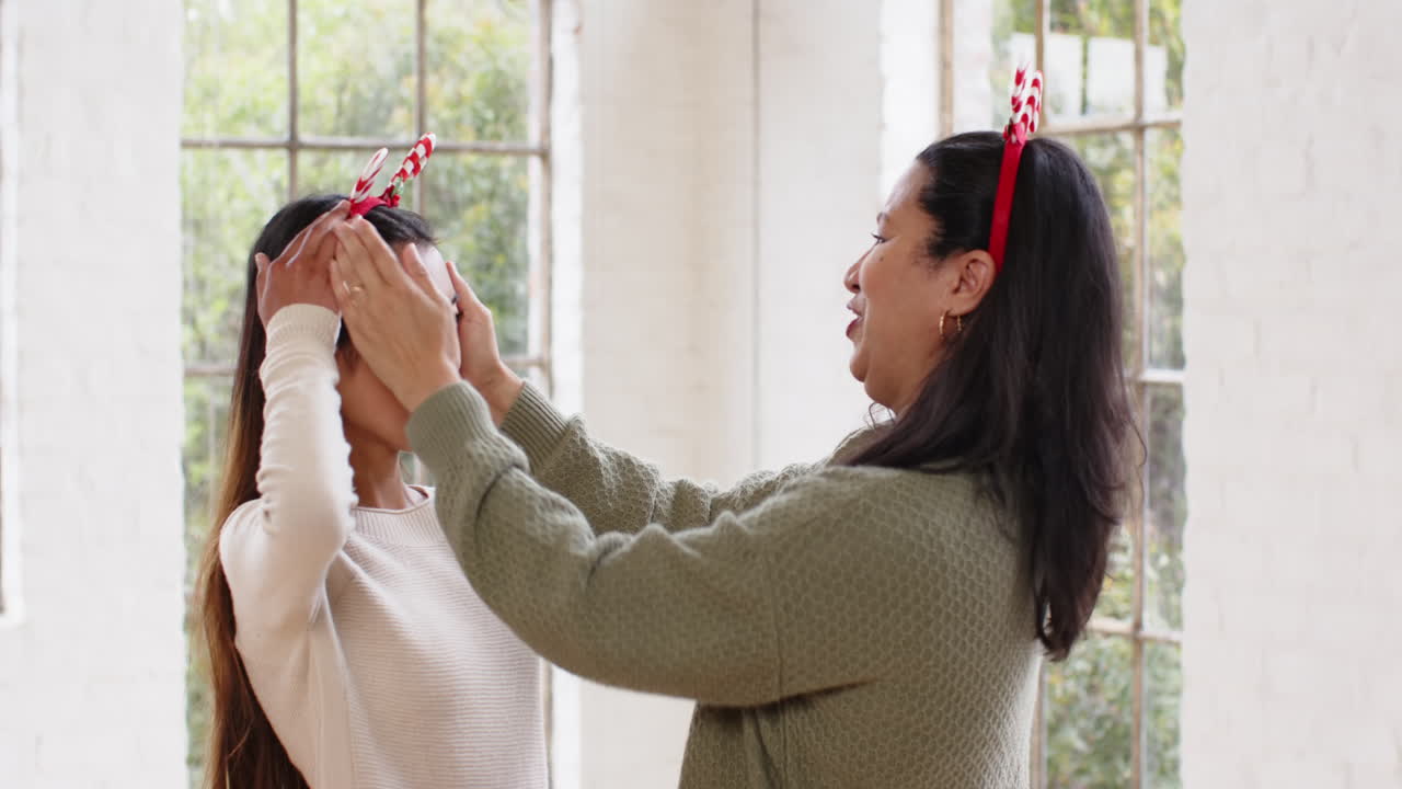 At christmas, asian grandmother and granddaughter wearing festive headbands sharing moment at home