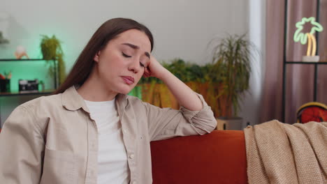 a woman sits on a couch and looks away, appearing sad and thoughtful.