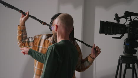 Male-Sound-Recordist-And-Camera-Operator-Working-On-Film-Set-Shooting-Movie-Or-Video-In-Studio-4