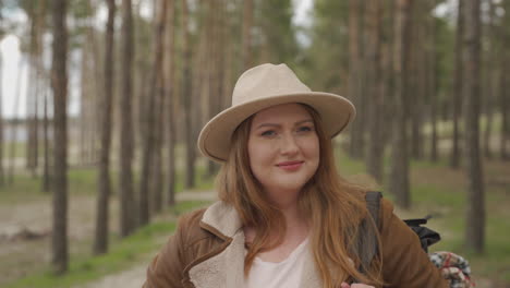 an adventurous curvy red haired female walking happy through the trees of a forest