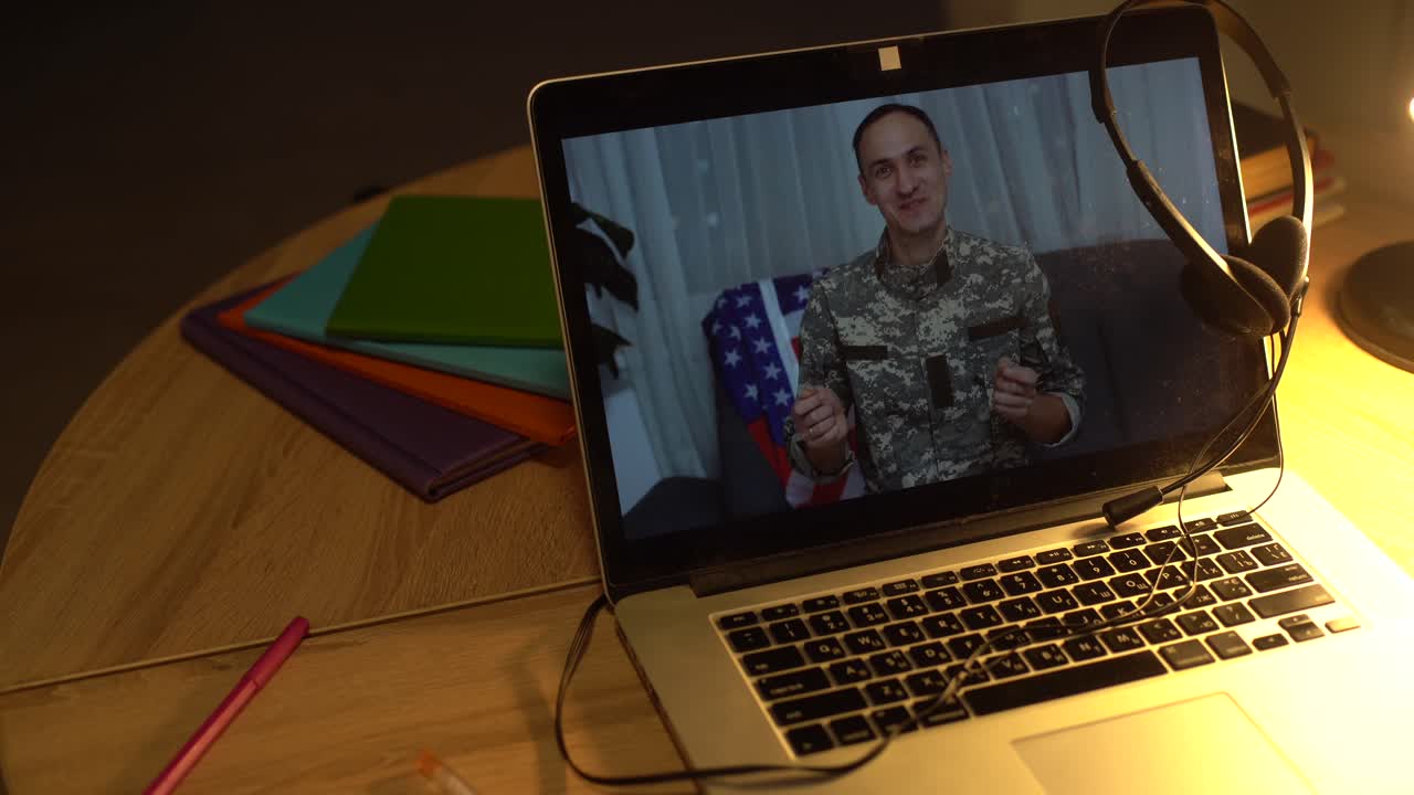 Brunette soldier man waving hand while making conference call on laptop indoors.
