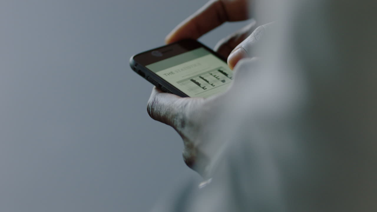 primer plano hombre de negocios afroamericano que usa un teléfono inteligente navegando datos de investigación en línea leyendo información de proyecto de mercado estudiante viendo estadísticas de desarrollo de empresas emergentes en la pantalla de su teléfono móvil