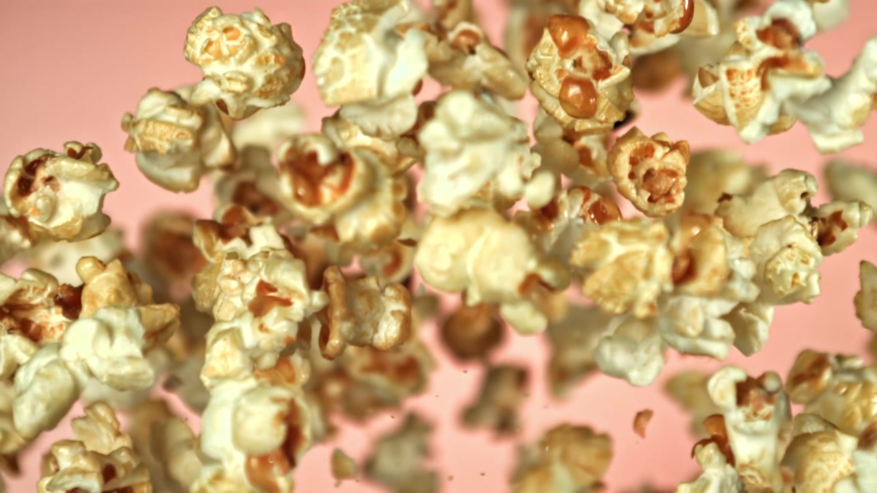 Palomitas acarameladas volando y cayendo a cámara lenta sobre fondo rosa