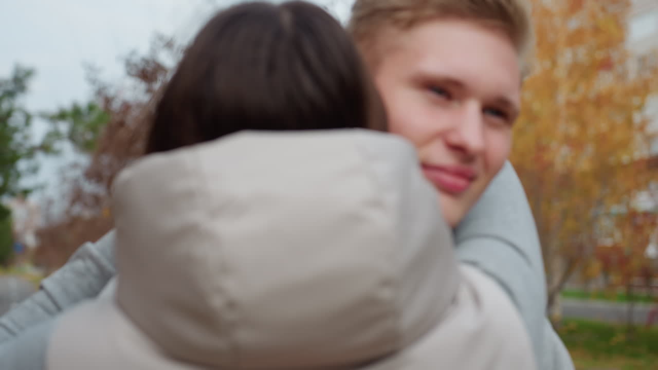 Couples dressed in summer jackets walk toward each other on tree-lined path during breezy day surrounded by autumn leaves ready to embrace warmly under soft daylight