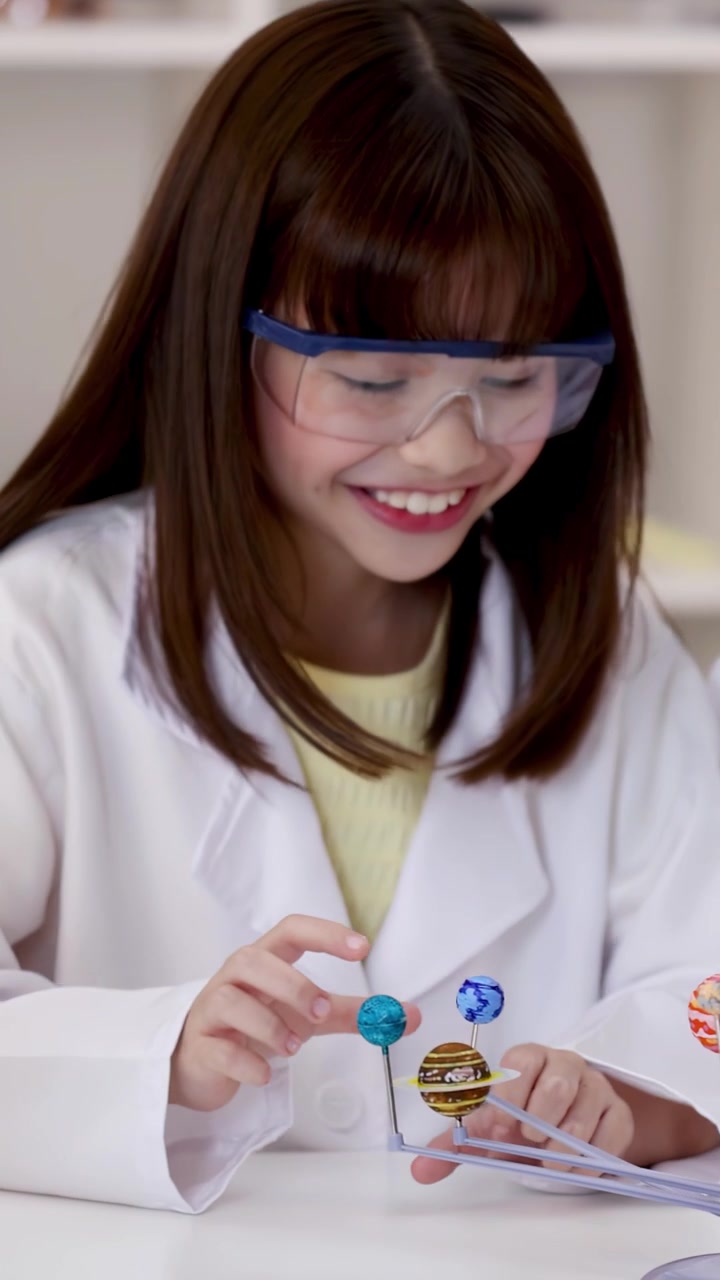 Young student wearing safety goggles interacts with planetary model during science class in bright classroom.