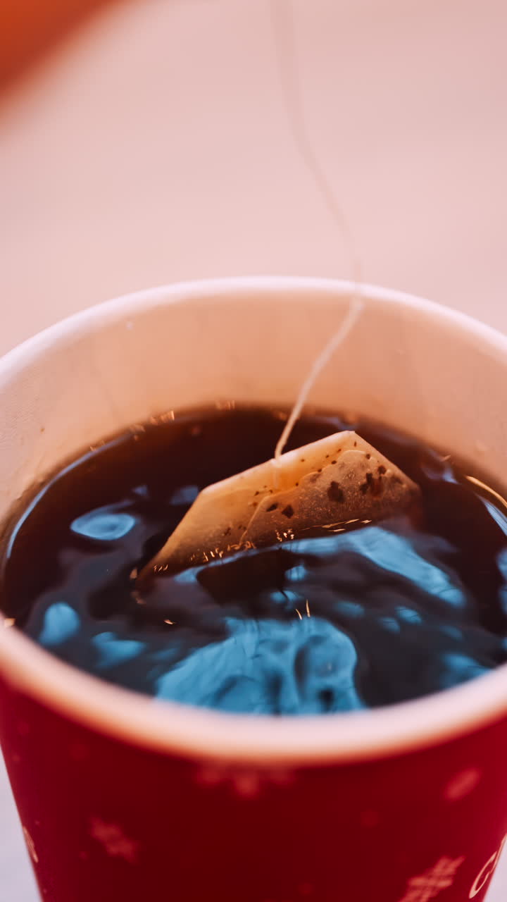 Close up of a tea bag brewing into a red cup with Merry Christmas writing on it. Vertical