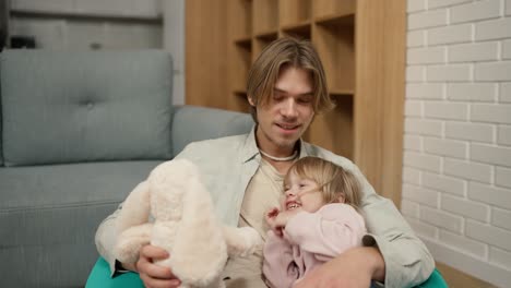 Father-and-daughter-play-together-with-soft-toy,-sitting-on-the-chair