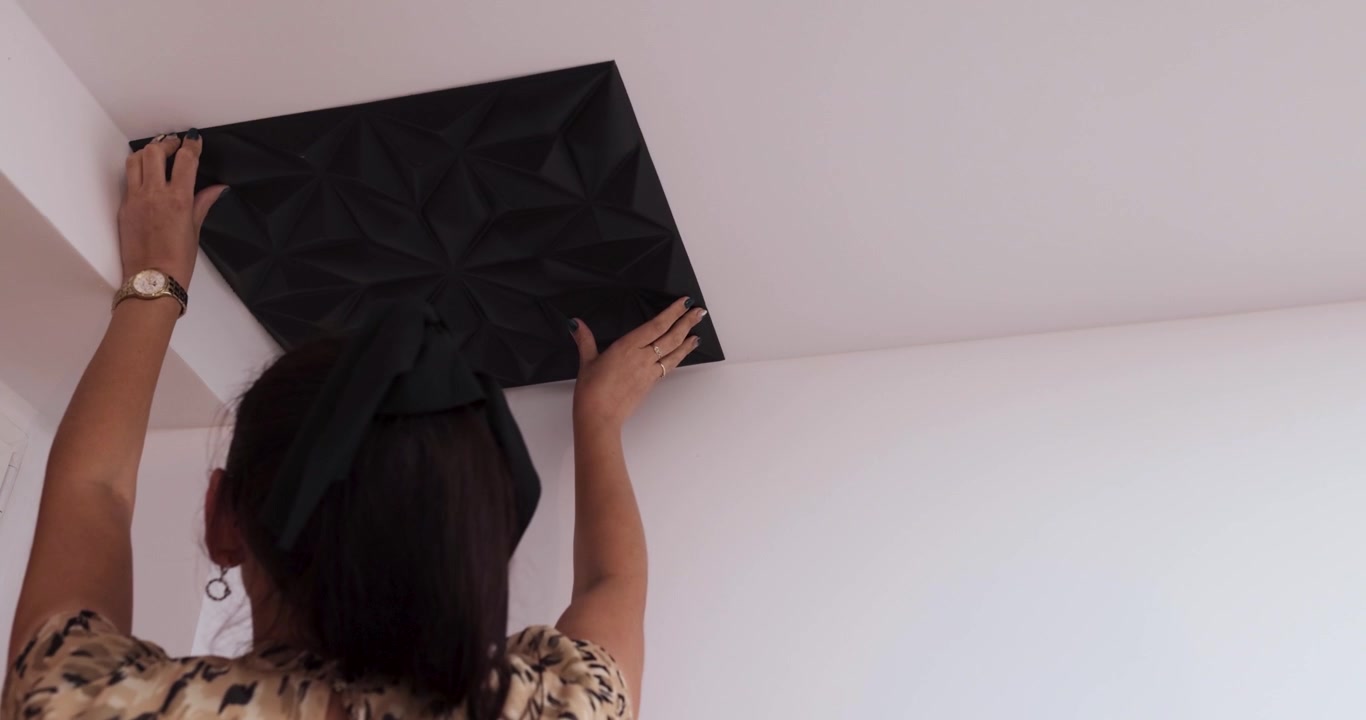 Giovane donna caucasica bruna con capelli raccolti e orologio d'oro che incolla un pannello nero sul soffitto bianco, ripresa 4K