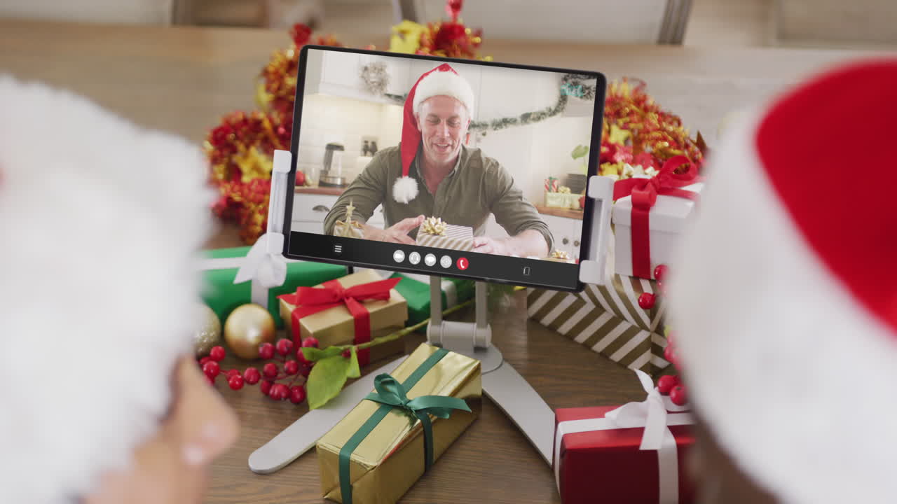 animación de una pareja diversa con sombreros de santa en una llamada de video de tableta con un hombre en navidad