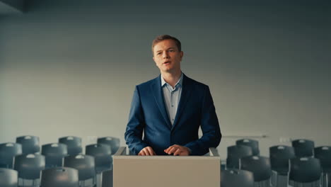 young man delivering a speech at a podium in an empty hall