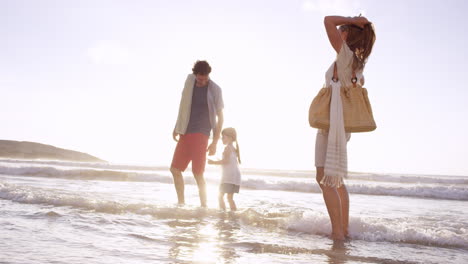 Familia-Feliz-Jugando-En-Las-Olas-En-La-Playa-Al-Atardecer-De-Vacaciones