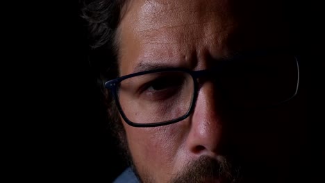 bearded man with glasses in the dark curiously looking at camera