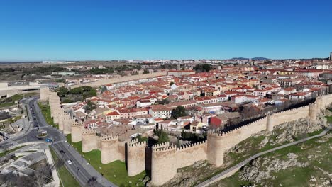 Vuelo-De-Orvita-Sobre-La-Ciudad-Patrimonio-De-La-Humanidad-Por-La-Unesco-Viendo-Sus-Murallas-Sur-Y-Su-Carretera-Con-Autos-Circulando-Y-Sus-Viviendas-Internas-En-Un-Día-De-Invierno-Con-Un-Cielo-Azul-En-Avila-españa