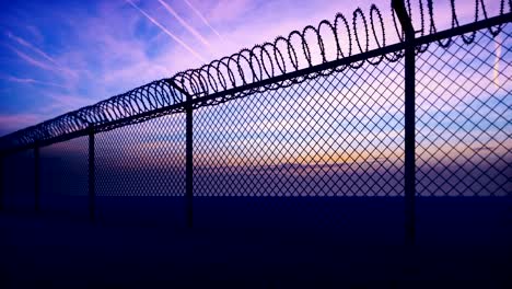 clouds and a sunset can be seen through the metal prison fence with barbed wire. loop realistic 3d animation.