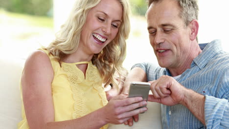 Happy-couple-using-smartphone-on-sofa