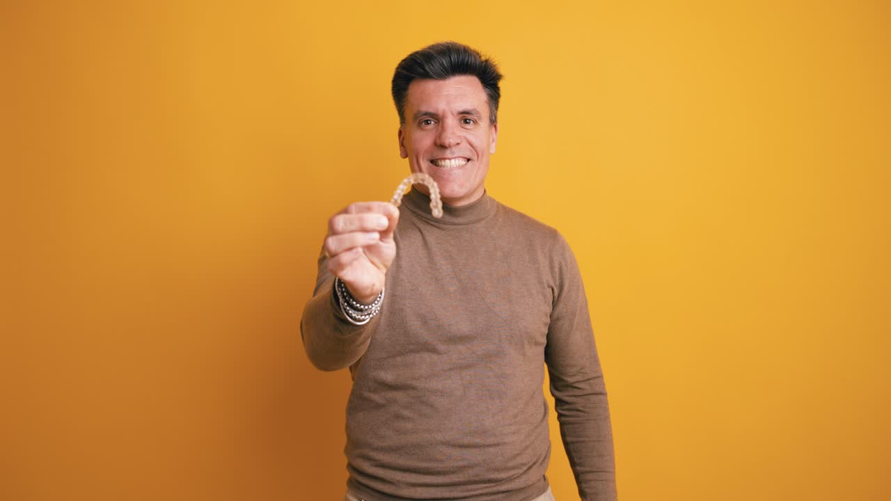 Uomo sorridente che tiene in mano un allineatore dentale trasparente