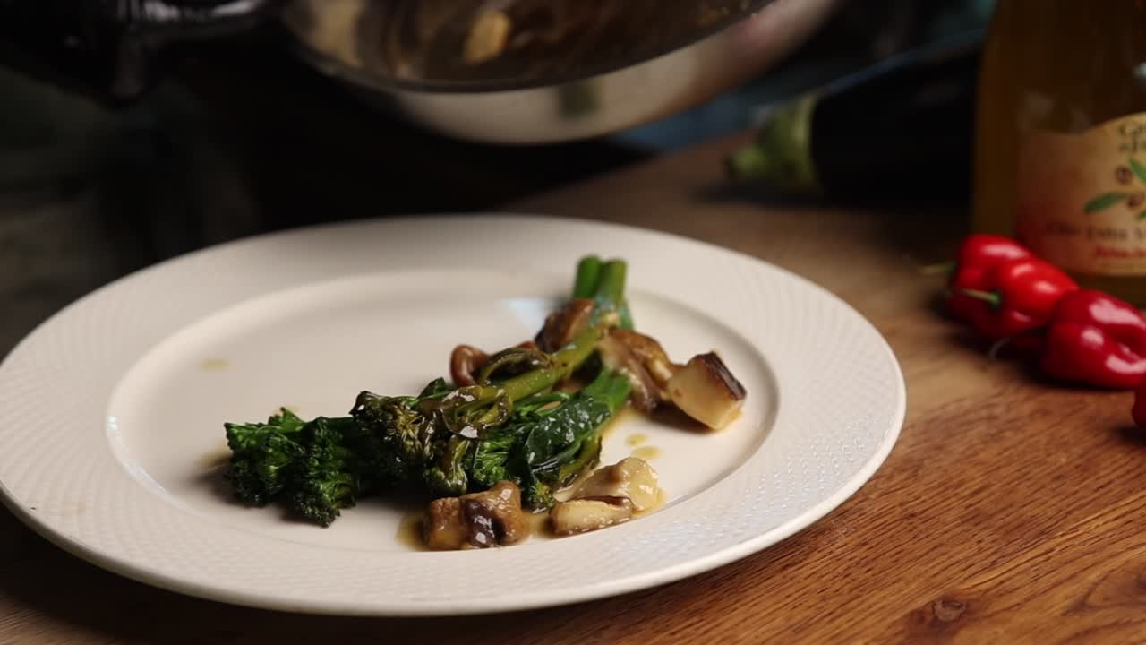 Chef Plating Cooked Broccoli and Mushrooms on a White Dish