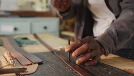 hands of african american craftsman using tools to make a hole in leather workshop