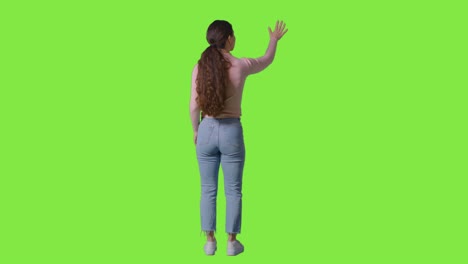 vista trasera de longitud completa toma de estudio de la mujer mirando alrededor del marco e interactuando con el entorno de la pantalla verde contra la pantalla verde