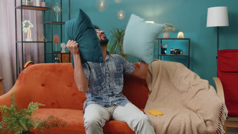 man laughing and having fun while fighting with pillows on a couch