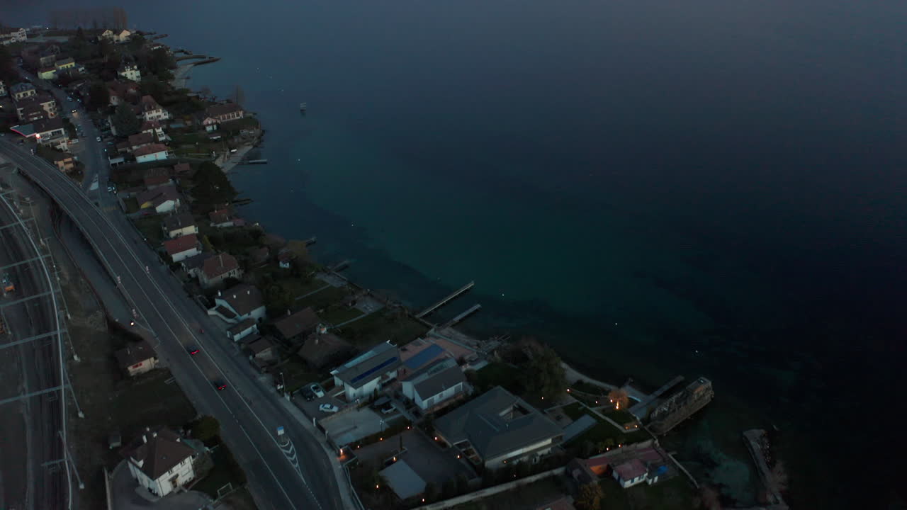Aerial of highway at the edge of small town, tilting up to beautiful lake at dusk