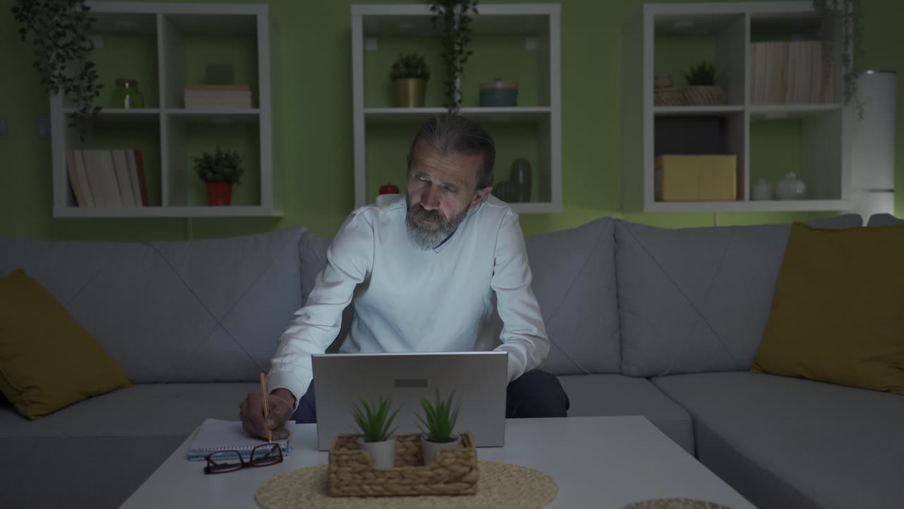 un hombre de mediana edad que trabaja en una computadora portátil experimenta un corte de energía en su casa.