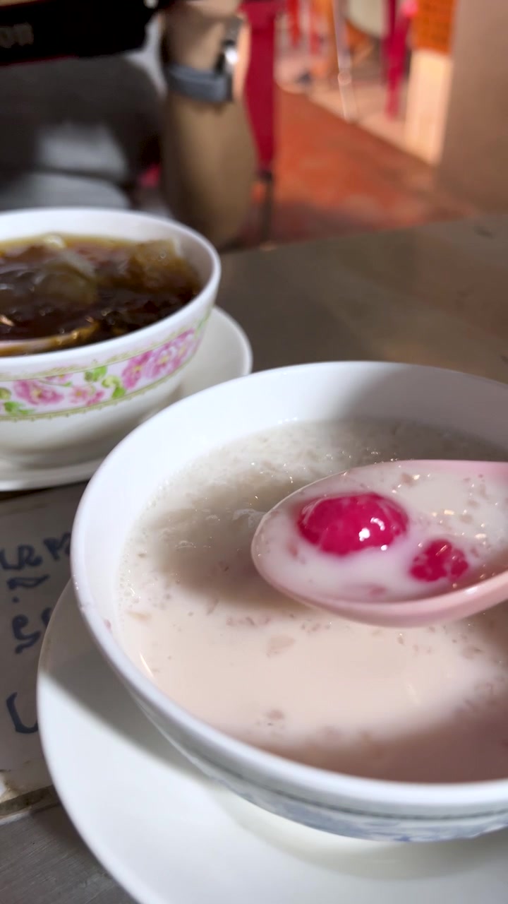 Tangan mengaduk hidangan penutup Thai red rubies dalam santan di bawah pencahayaan jalan yang terang, tampilan close-up.