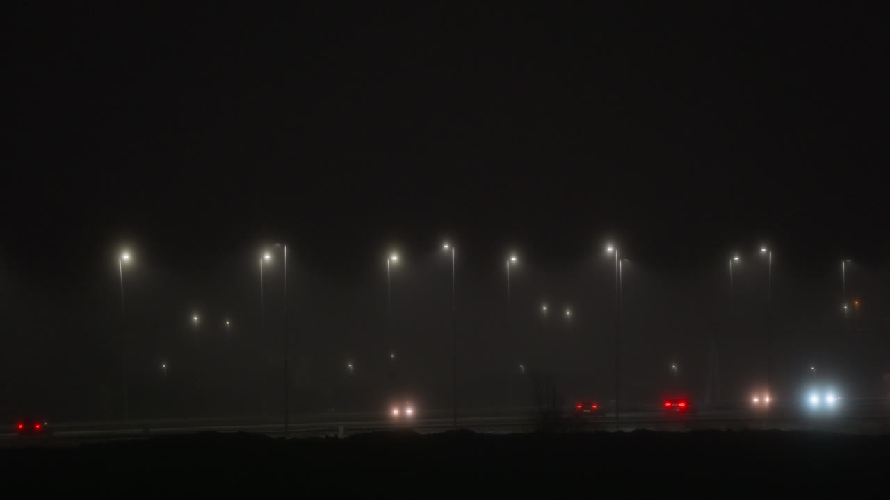 Cars Driving on Foggy Highway at Night with Streetlights