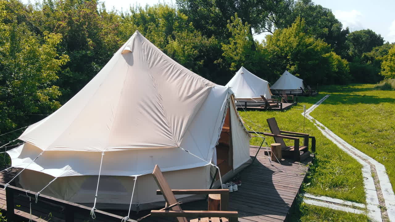 Glamping tents with chairs in the nature, green grass and trees, trail