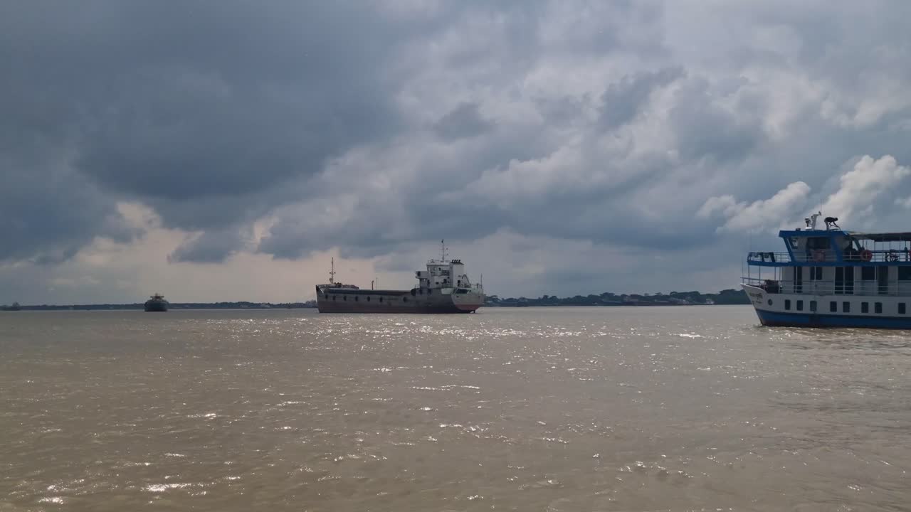 Boats anchored in the wide Pasur River delta where the water meets the Bay of Bengal, gentle waves under a cloudy sky during the rainy season in the Sundarbans, Bangladesh