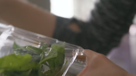 woman's hands pick through leafy greens in plastic container in slow motion