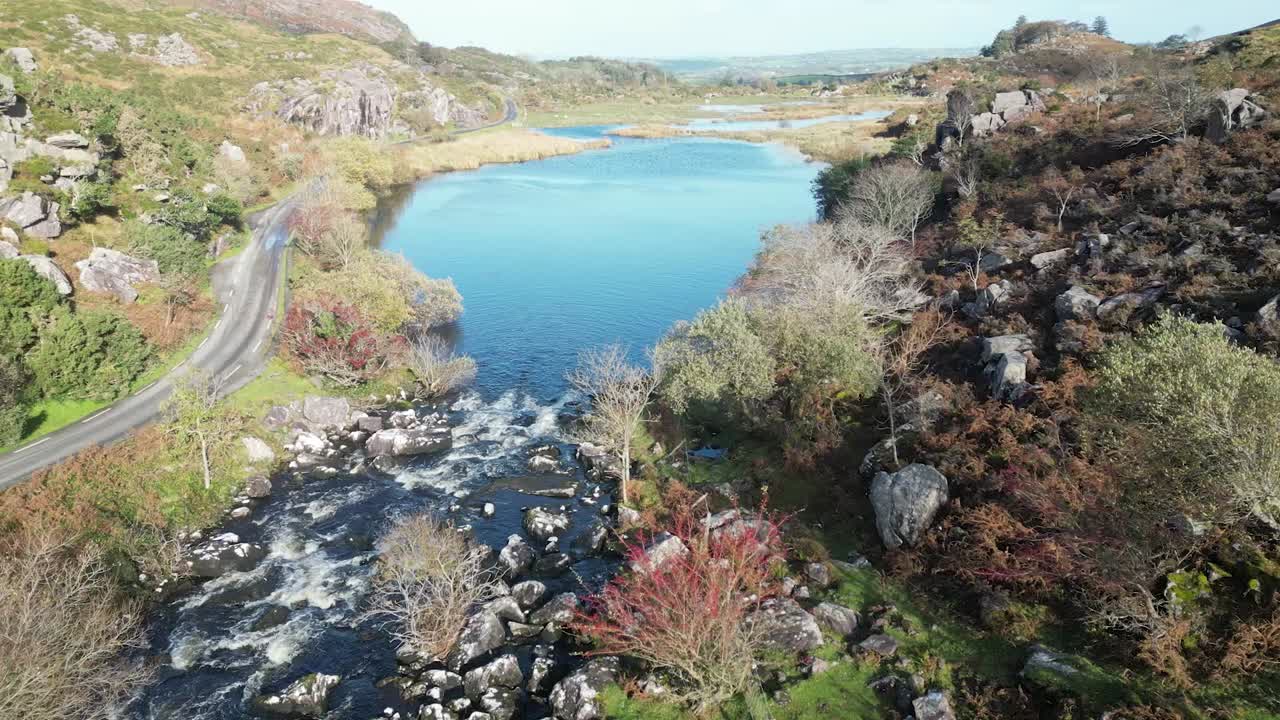 Wide drone shot of Gap of Dunloe, Bearna or Choim&iacute;n, mountain pass in County Kerry, Ireland, passing by trees descending towards the river