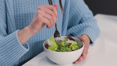 primer plano de una mujer irreconocible sentada en el escritorio y comiendo ensalada saludable